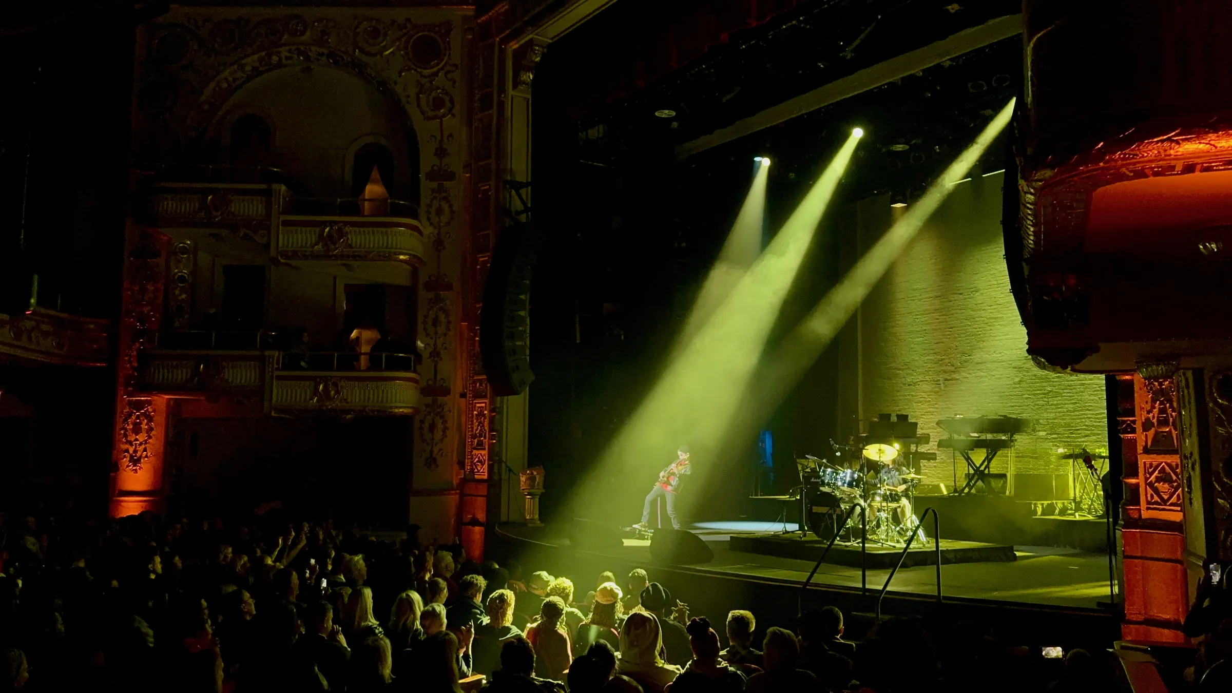 Aksel McDermott playing guitar under stage lights in a packed historic theater
